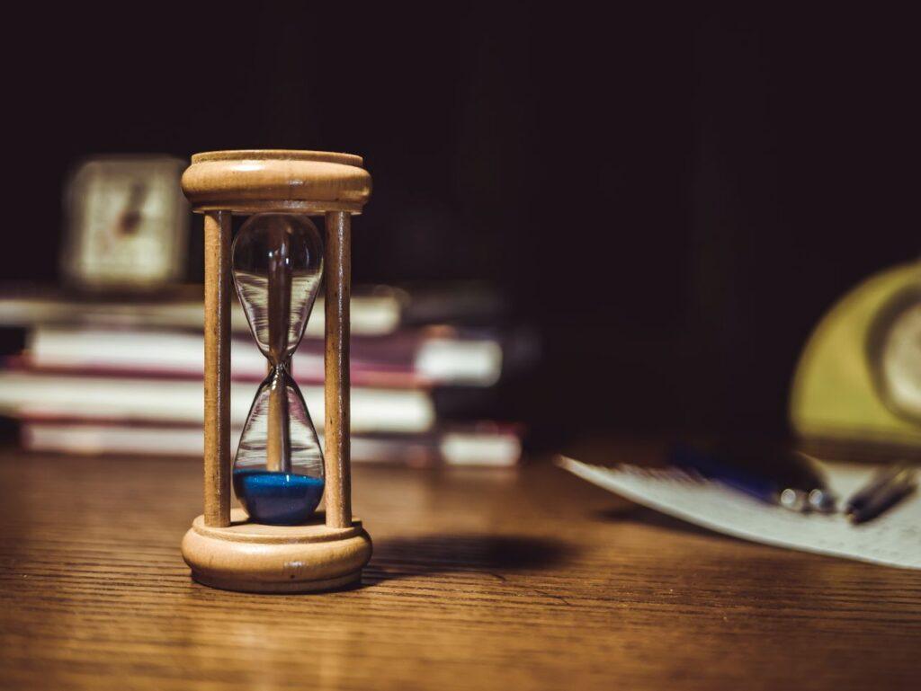 Eine Sanduhr auf einem Holztisch im warmen Licht – Sinnbild dafür, nicht mehr auf „irgendwann“ zu warten, sondern jetzt zu handeln