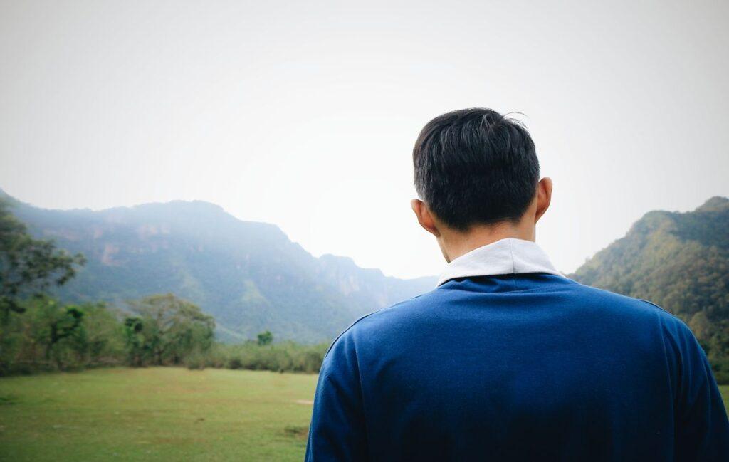 Ein Mann sitzt allein und ruhig auf einer grünen Wiese, den Blick in die Ferne gerichtet – Sinnbild dafür, aufzuhören sich mit anderen zu vergleichen
