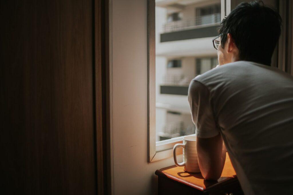 Ein Mann denkt mit einer Tasse am Fenster über seine nächsten Lebensschritte nach