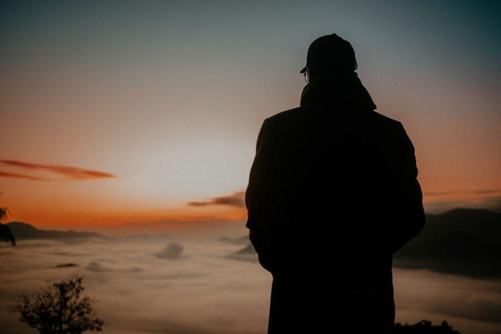 Silhouette eines Mannes, der ruhig auf den Sonnenaufgang über den Bergen blickt – Sinnbild für einen neuen, gelassenen Blick auf die zweite Lebenshälfte
