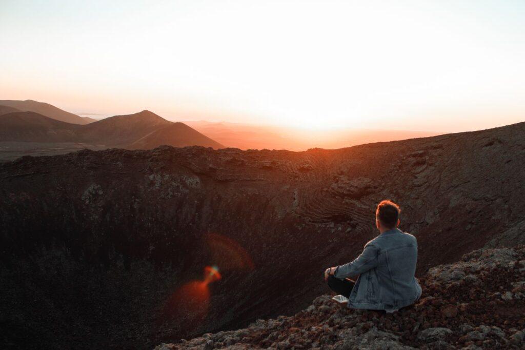 Ein Mann blickt am Rand eines Vulkankraters in den Sonnenaufgang und erlebt einen persönlichen Weckruf