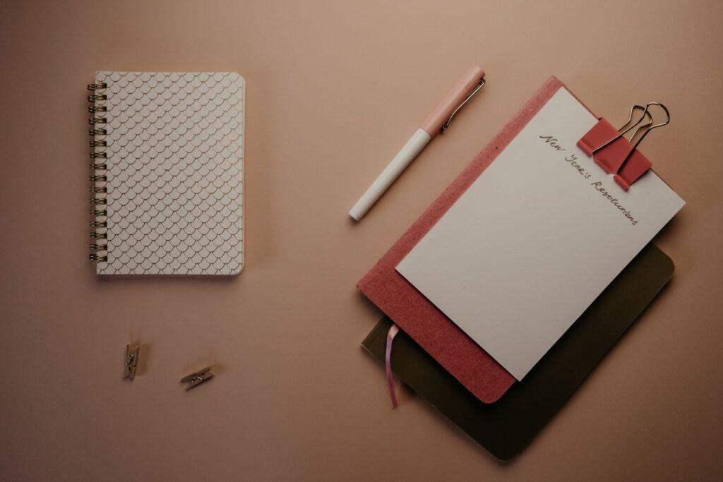 Notizbücher und Stift ordentlich auf einem Tisch arrangiert – Sinnbild für die HAT-vs-WILL-Übung, um herauszufinden, was man wirklich will